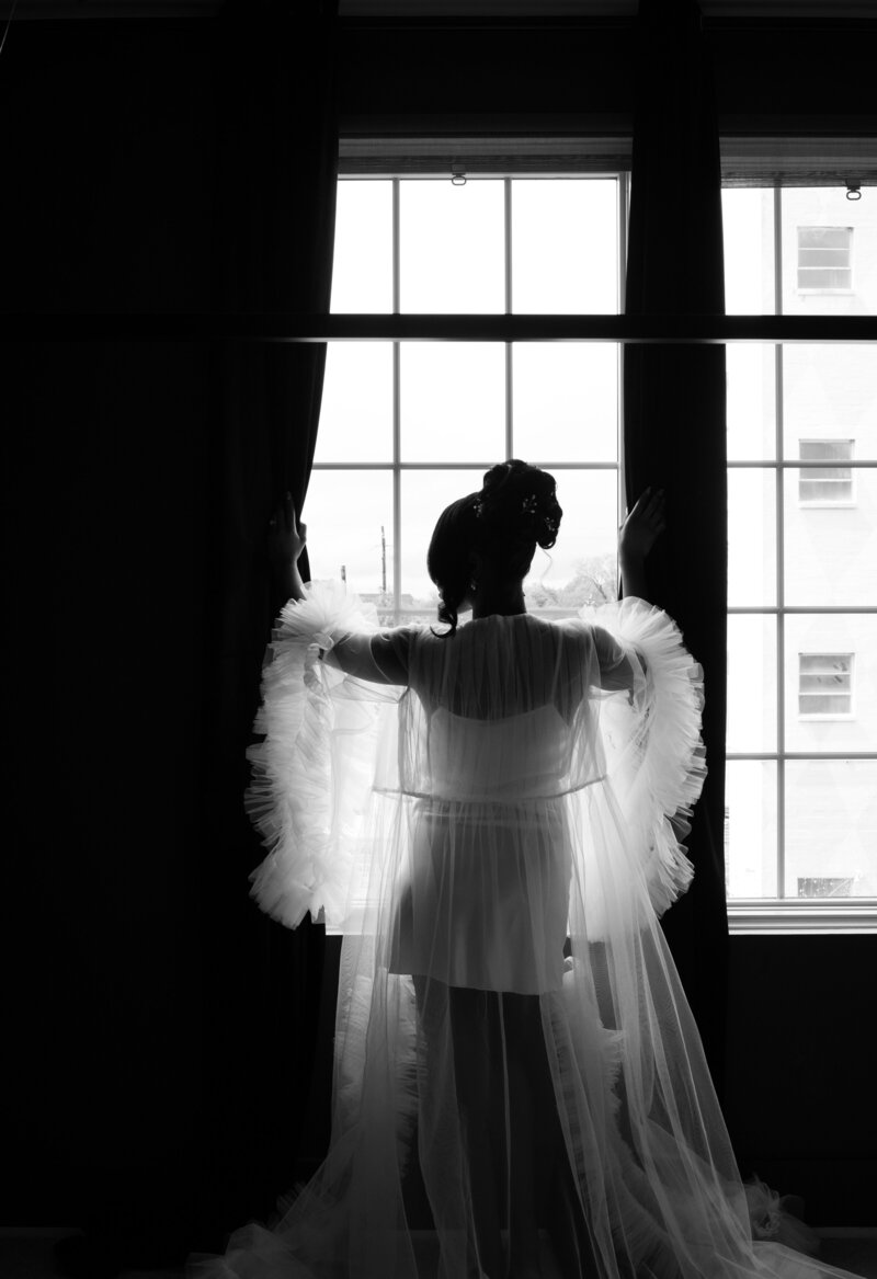 A black and white image of a woman in a white robe standing in the window