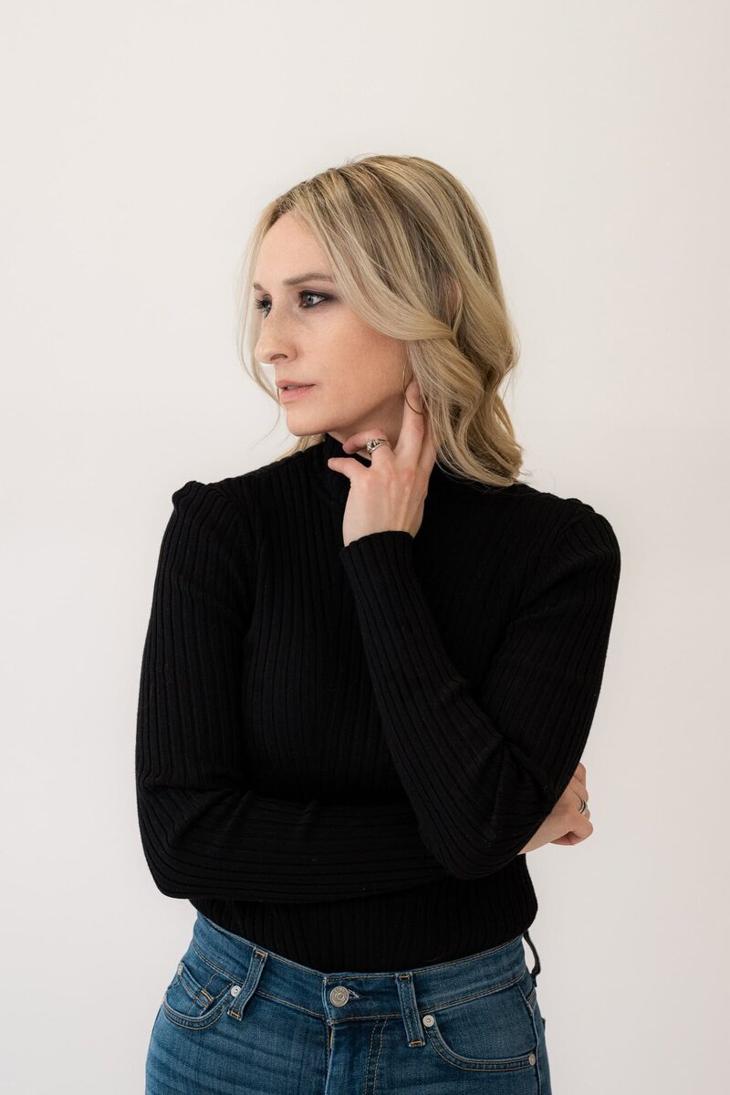 Joy Steele in a black turtleneck and jeans posing confidently, highlighting her skills as a Phoenix boudoir photographer.