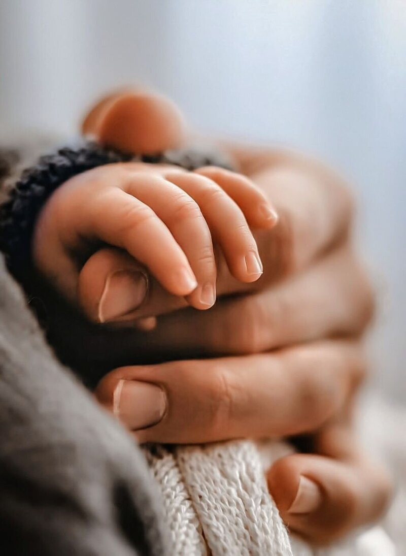 De hand van een volwassene omvat zachtjes de hand van een pasgeboren baby