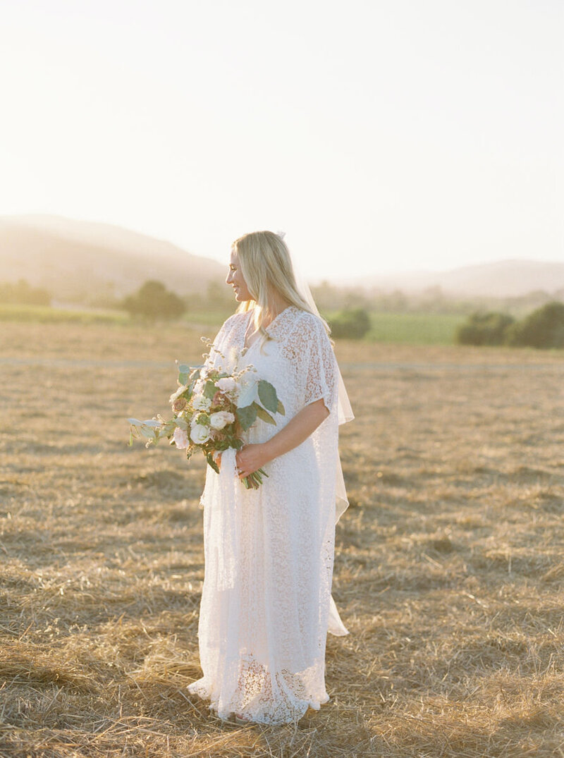 bride with lace dress and white bouquet standing in a field