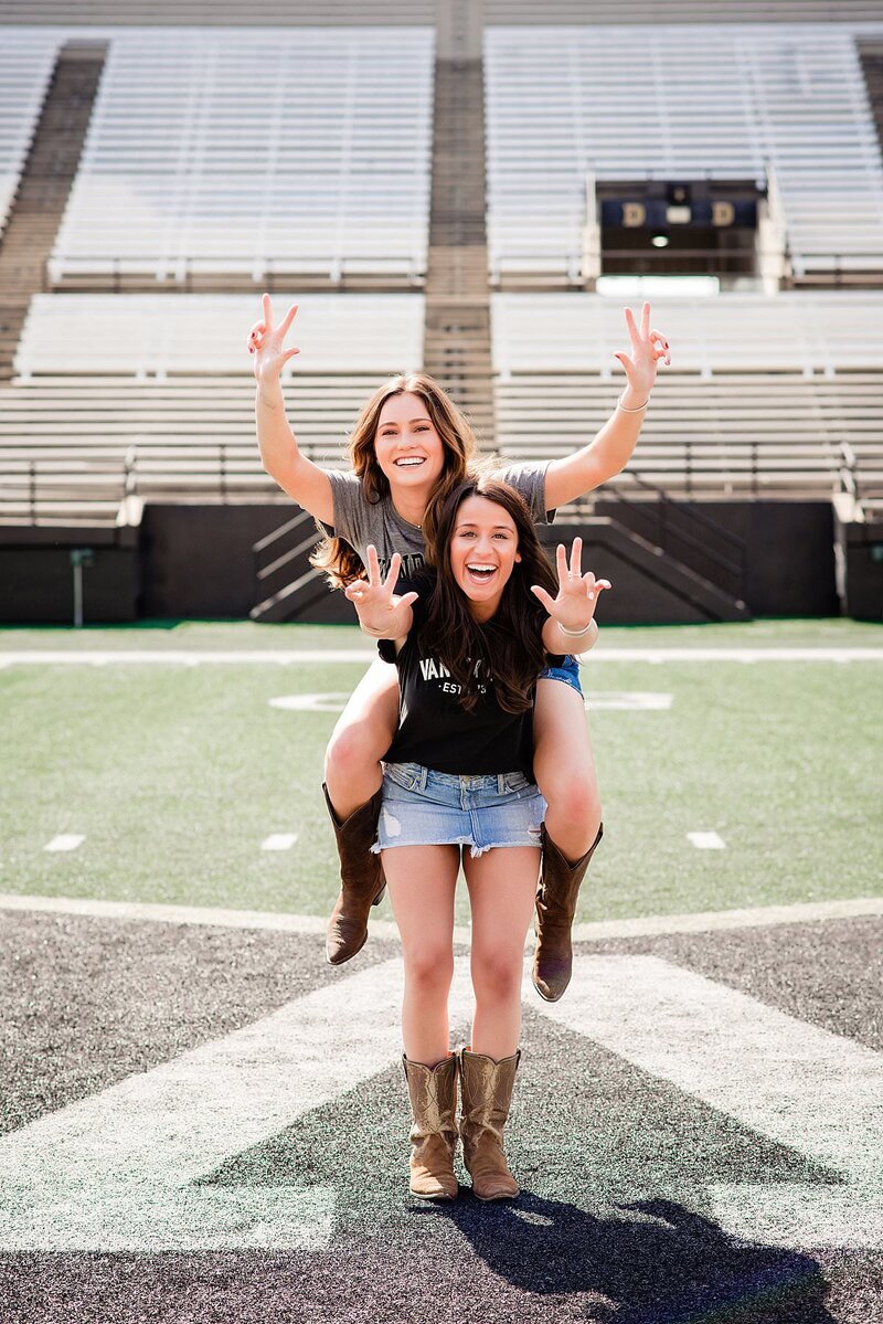 Two senior girls wearing Vanderbilt college shirts, sharing a piggyback ride and smiling at the camera
