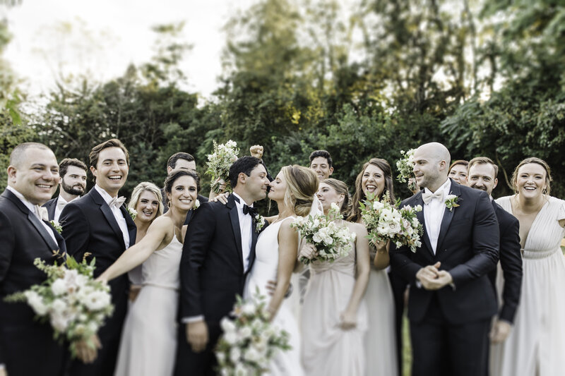 bride and groom looking at each other with their bridal party. men are wearing tuxes and bridesmaids are wearing blush dresses