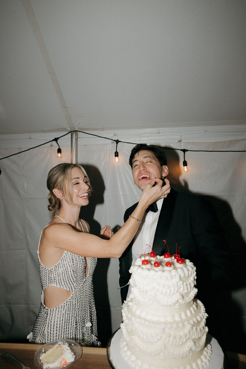 bride feeding cherry to groom before they cut their wedding cake at wedding reception 