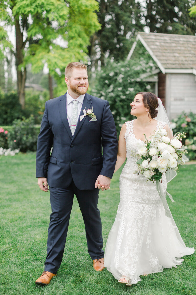 bride and groom holding hands and walking towards the camera while looking at each other and smiling