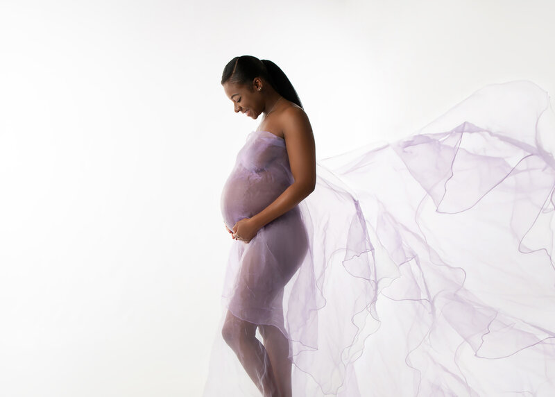 Charlotte, NC Expecting Black Mom in a Purple fabric  dress to give the illusion of coverage created in studio on a white background