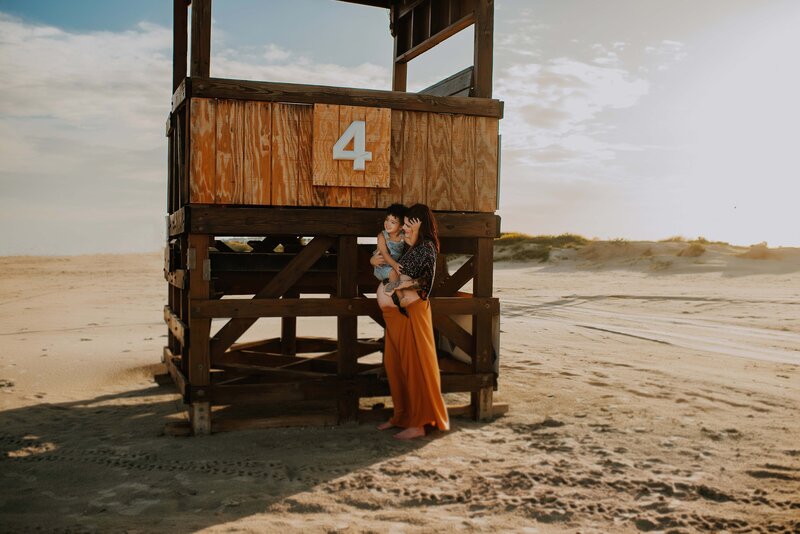 Expecting mother holding her son by a lifeguard stand at Galveston beach.