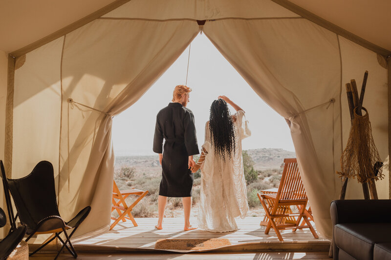 couple stands in the door of their canvas tent in Moab on the morning of their elopement