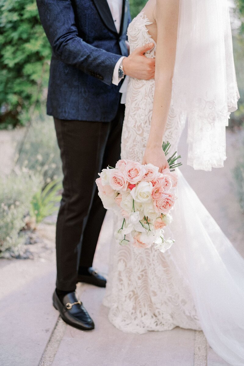 groom-hugs-bride-with-bouquet-around-waist-while-standing-garden-cropped-faceless