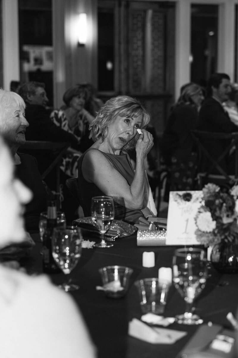 Black and white photo of wedding guest dabbing tears during reception speeches – emotional candid moment documented by Colorado wedding photographer