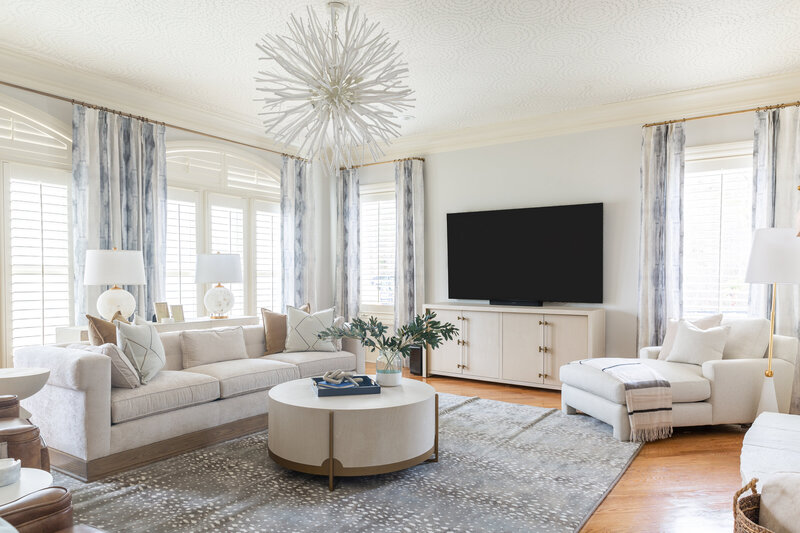 Elegant living room with a modern chandelier, neutral-toned furniture, and a sleek entertainment setup.