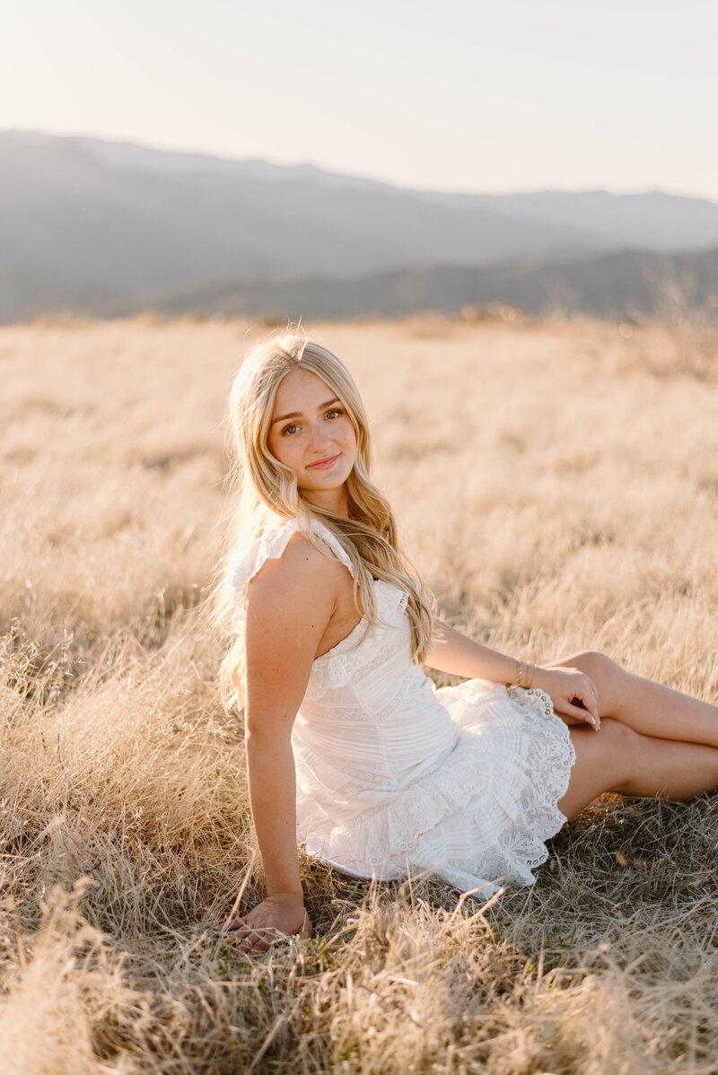 High school senior girl sitting in a wheat field wearing a white dress