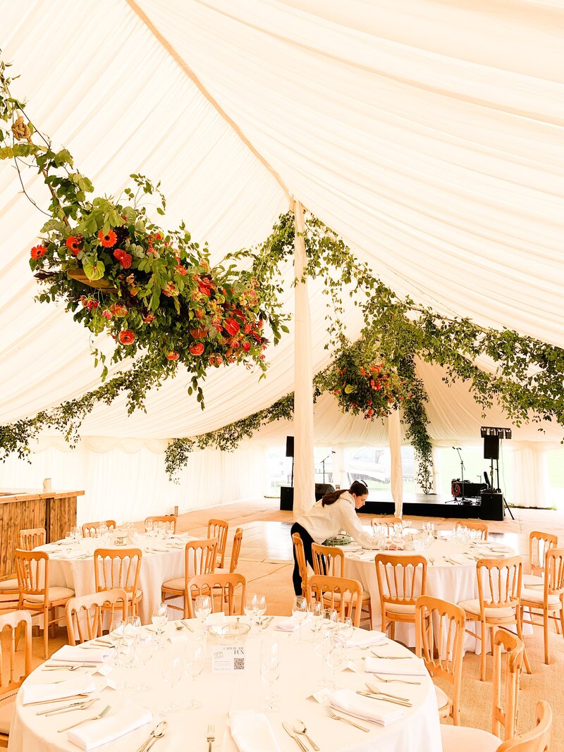 Anna Sawle is arranging a large display of flowers on a glass vase in the marquee. The flowers include coral charm peonies, purple orchids 