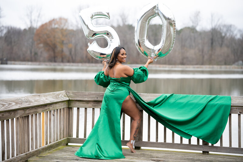 50th milestone birthday photoshoot woman wearing green ball gown by a lake