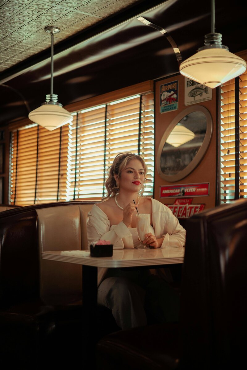 A woman wearing white sitting at a diner booth, representing the fun and quirky inspirational vibes of the bridal show.