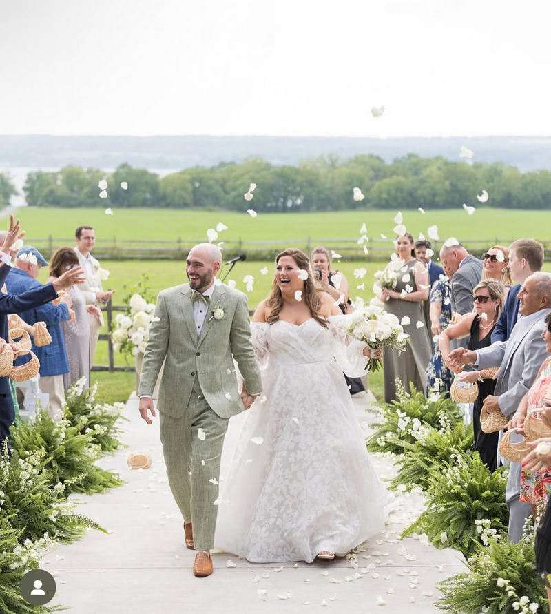 Bride and groom walking back down the aisle with petals in the air while wedding guests cheer.