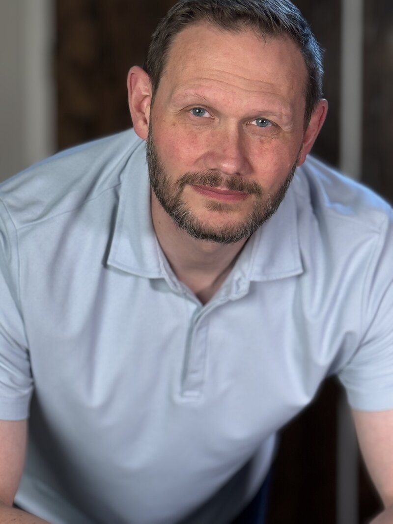 Sincere middle-aged man with a serious expression, leaning forward to engage in a conversation—symbolizing dedication and confidence. Ideal image for a Peace Coaching website promoting emotional wellness, stress relief, and personal growth