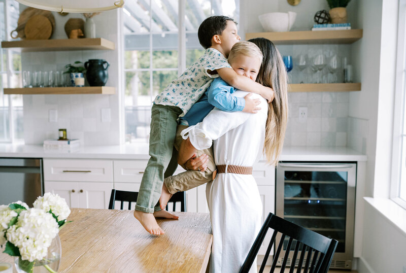 Two little boys jumping into mom's arms while in their kitchen during a family photo session with Allison Krogness Photography.