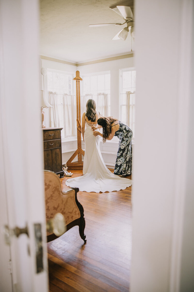 Mother of the brides helping the bride zip up her wedding dress