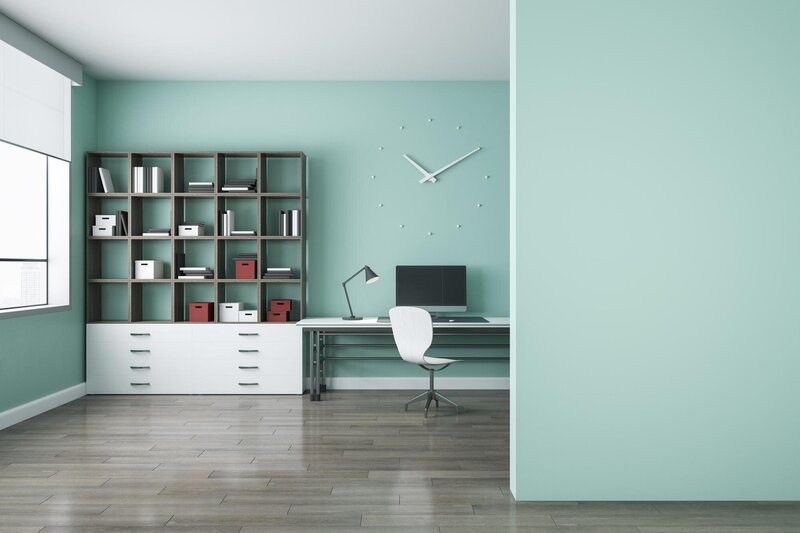 Modern office with open shelving, organized storage boxes, a desk with a lamp and computer, and mint green walls.