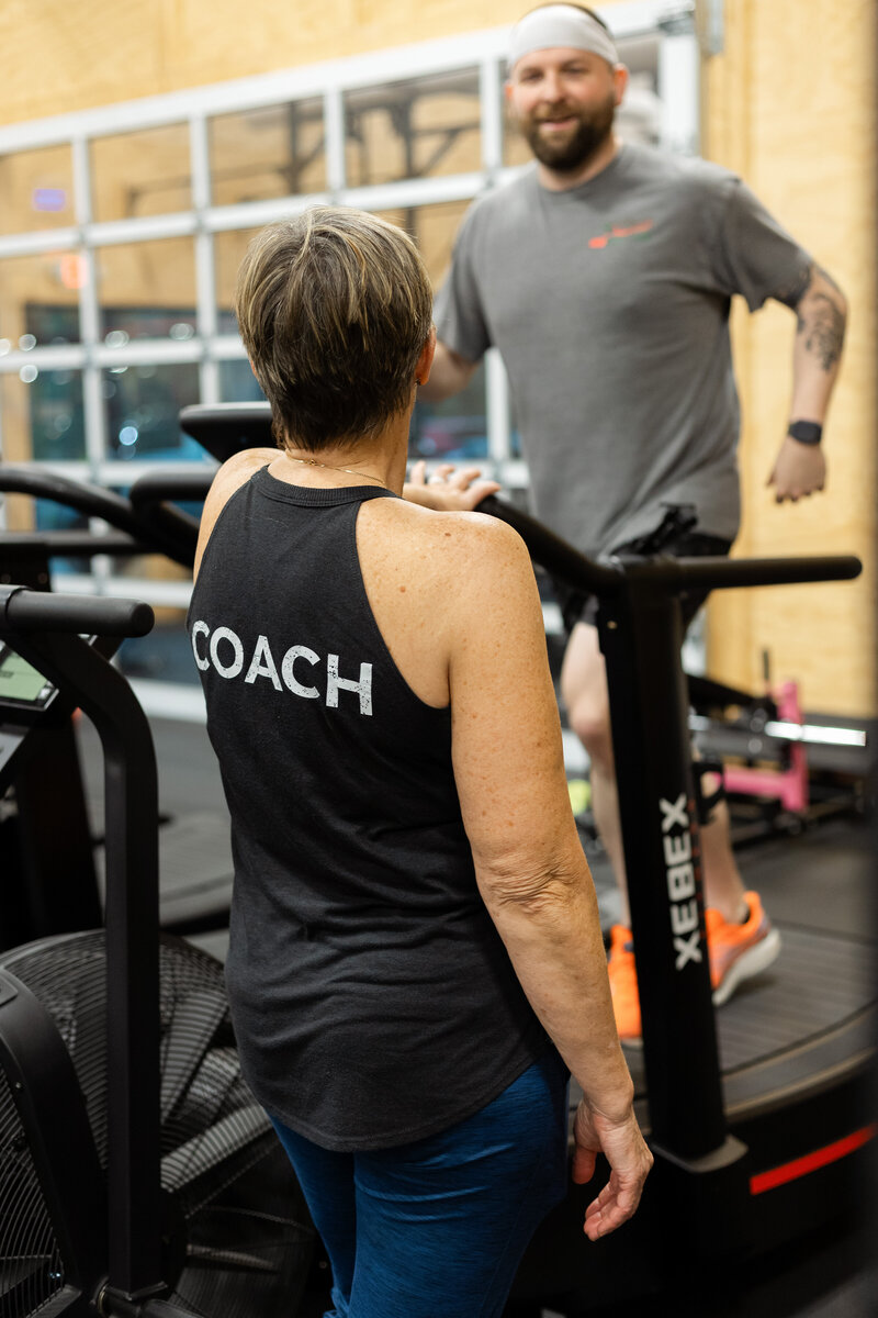 Coach Mary at Skopos Athletics in Dundas, MN, providing guidance and support to a gym member during a workout session.