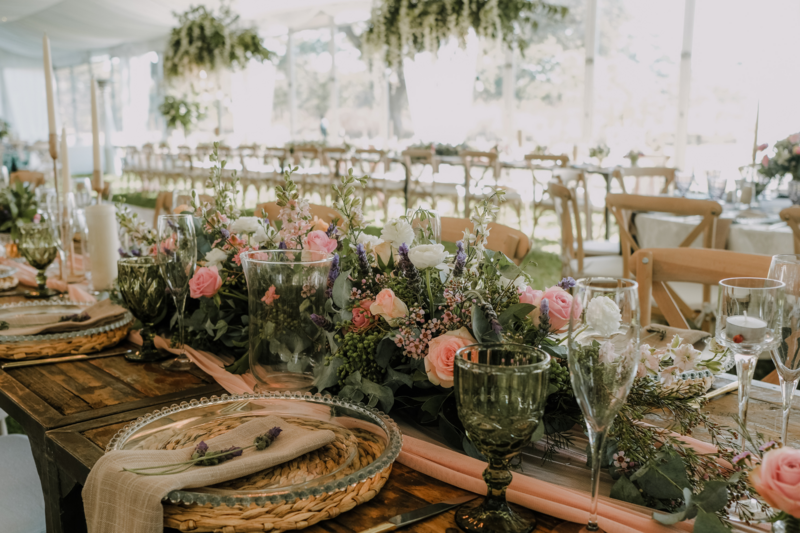 At the wedding reception, tables are adorned with enchanting arrangements featuring blush tones and lush greens, creating a scene of refined elegance. Each table centerpiece is a masterpiece of floral artistry, boasting delicate blush roses, soft peonies, and verdant eucalyptus leaves. The blooms are nestled in vintage-inspired vases or rustic wooden boxes, adding a touch of charm and sophistication to the decor. Sprigs of greenery cascade gracefully from the arrangements, intertwining with fairy lights or candles, casting a warm, romantic glow. Against the backdrop of crisp white linens and shimmering tableware, the blush and green hues evoke a sense of freshness and tranquility, inviting guests to revel in the beauty of the celebration.