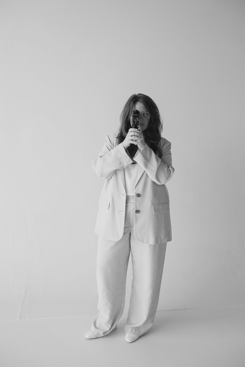 A woman dressed in a white suit and white shoes stands confidently, exuding elegance and professionalism.