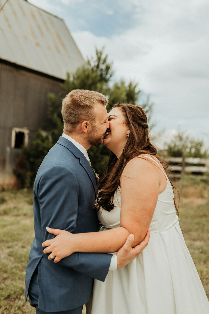 newlyweds kissing in front of barn