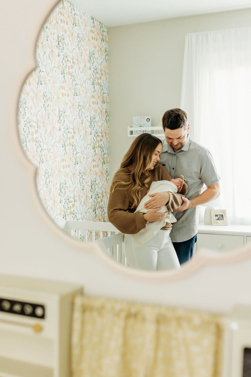 Two parents snuggle and admire their newborn baby inside a cheerfully decorated nursery, photographed be a Vancouver Washington newborn photographer