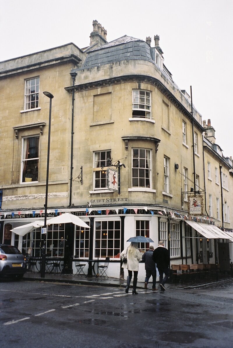 Portrait photo of an old building on a rainy street with people walking by with an umbrella