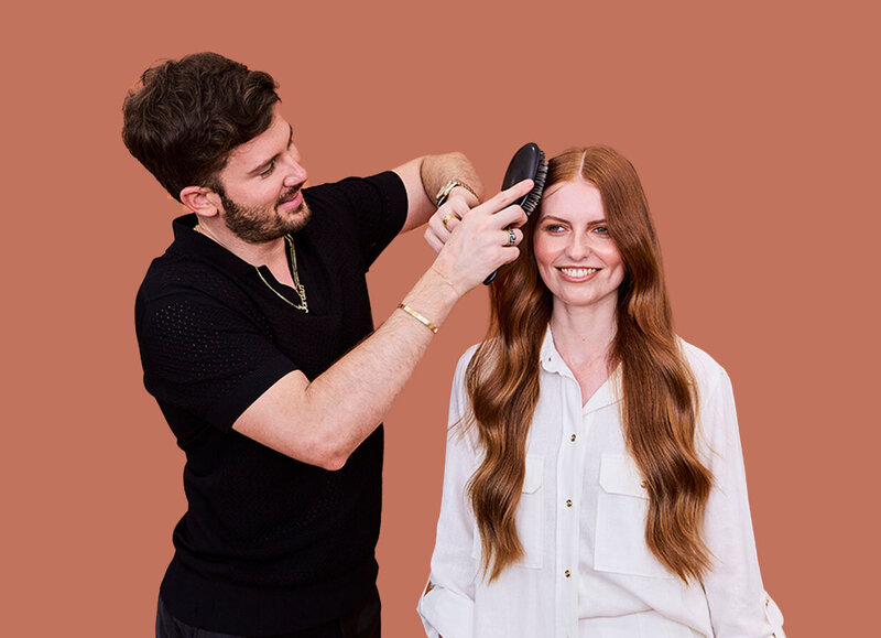 Hairdresser styling long, red waves with a brush in a modern salon, showcasing professional hairdressing techniques.