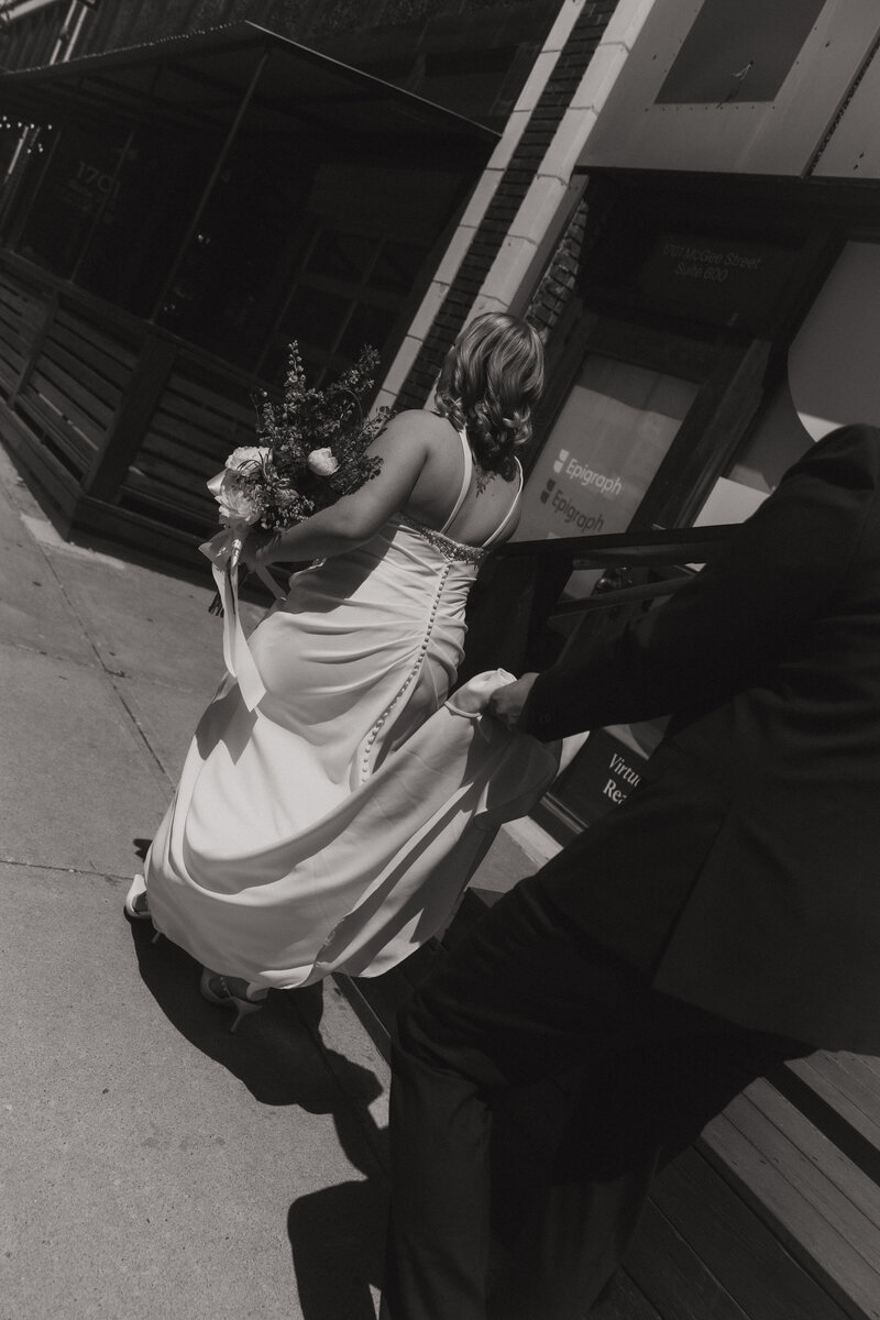 Bride walks away holding a bouquet while the groom holds her train