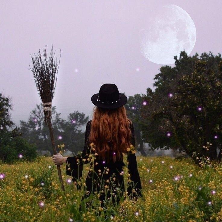 One of the Witchcraft teachers at The Magickal Path School standing in a field with a broomstick beneath a full moon