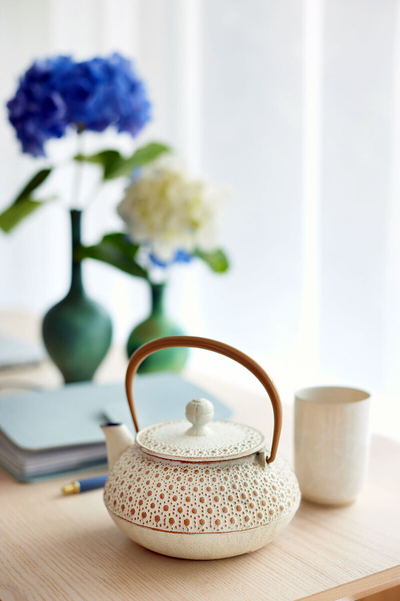 close up of a white Japanese teapot with a notebook and flowers in the background