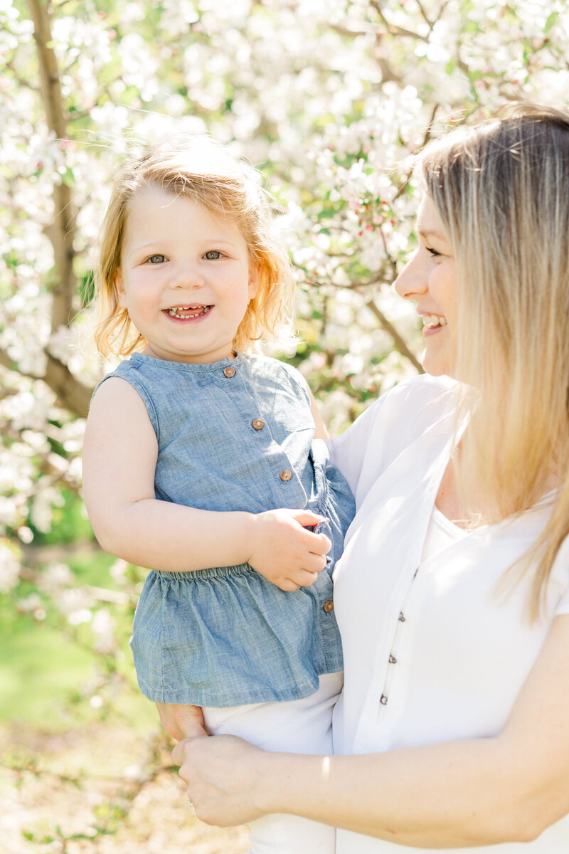 a toddler is held by her mother while smiling at the camera for Minneapolis Portrait Photography session