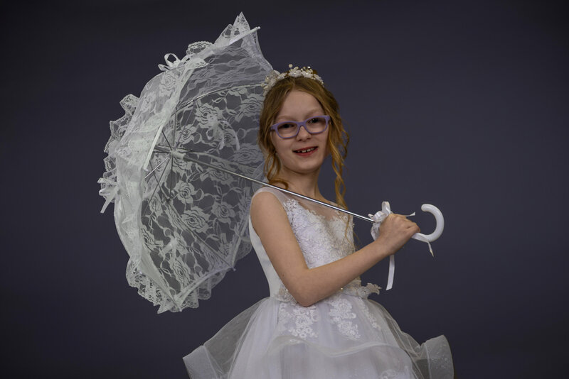 A communion girl with a parasol with a purple backdrop