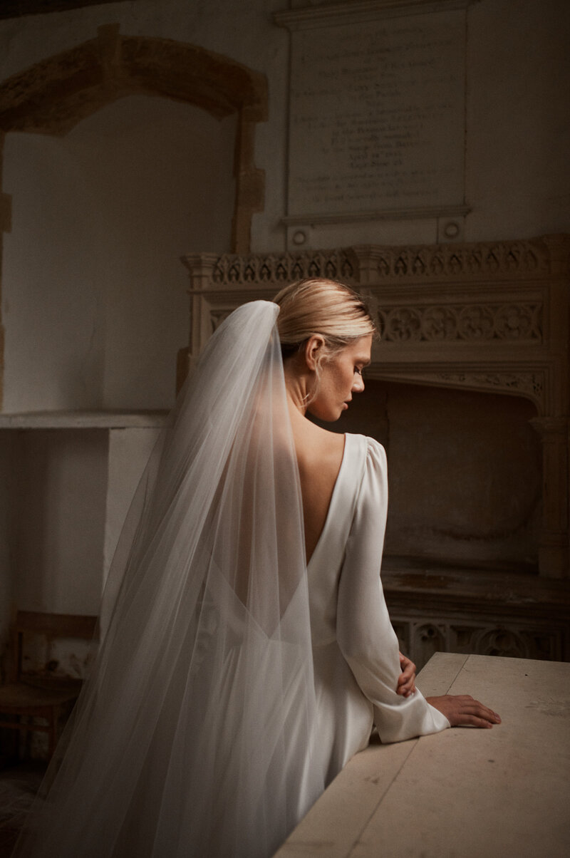 Long-sleeved silk wedding dress with deep v back worn by bride at wedding in church