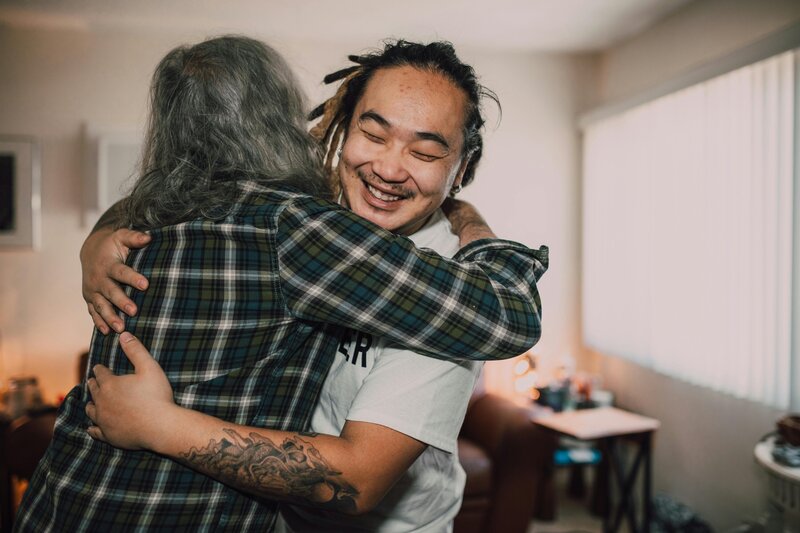 Two people smiling and hugging warmly inside a home, showing comfort and connection.