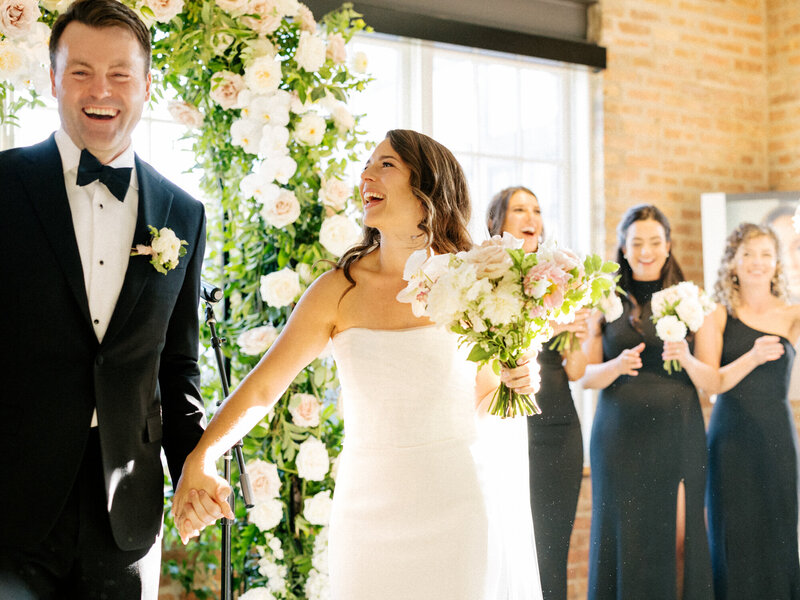 A newlywed couple beaming with happiness as they walk back down the aisle at Morgans on Fulton, surrounded by celebrating guests.