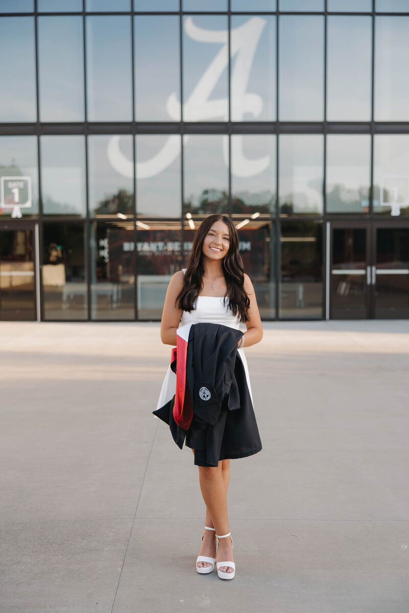 Student at the university of alabama taking graduation pictures in front of Bryant Denny Stadium with her masters regalia