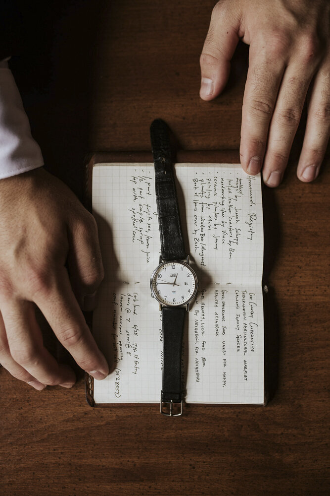 flat lay of a groom's watch laying across his vow and prayer book