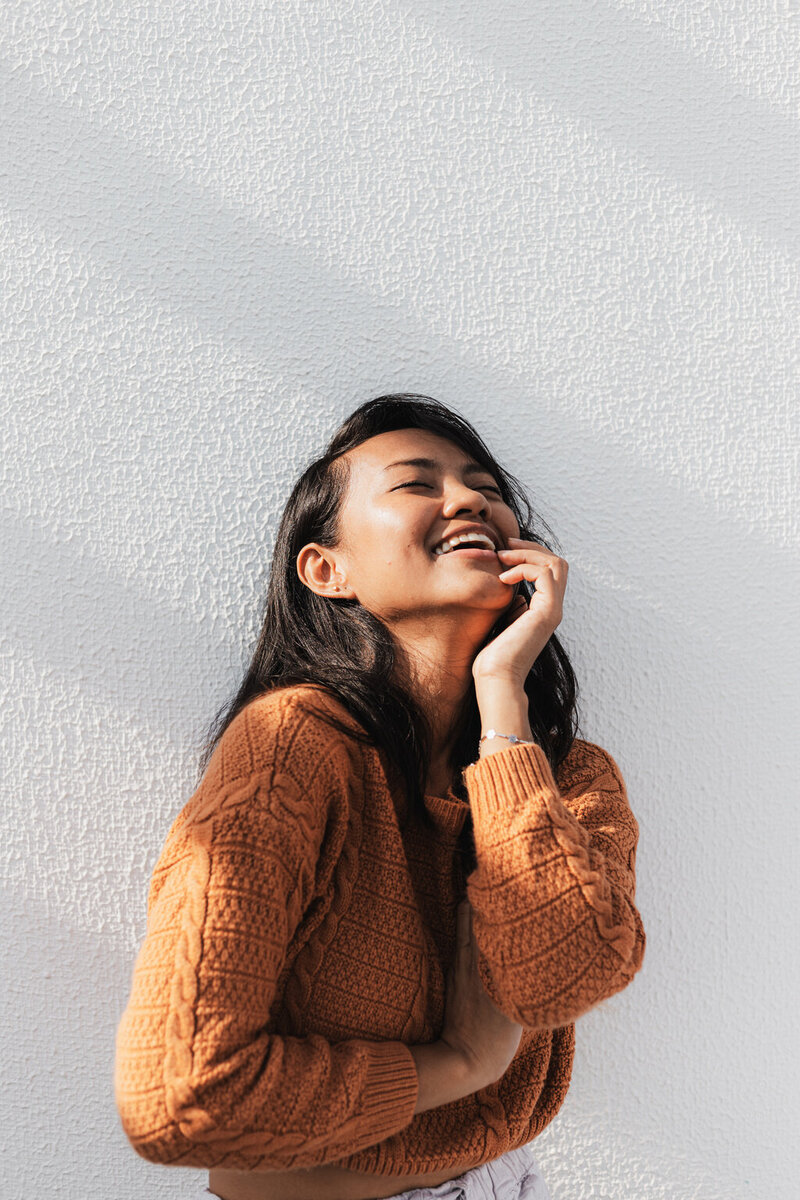 Confident young woman smiling in an orange sweater, evoking warmth and emotional resilience through somatic therapy in Manhattan.