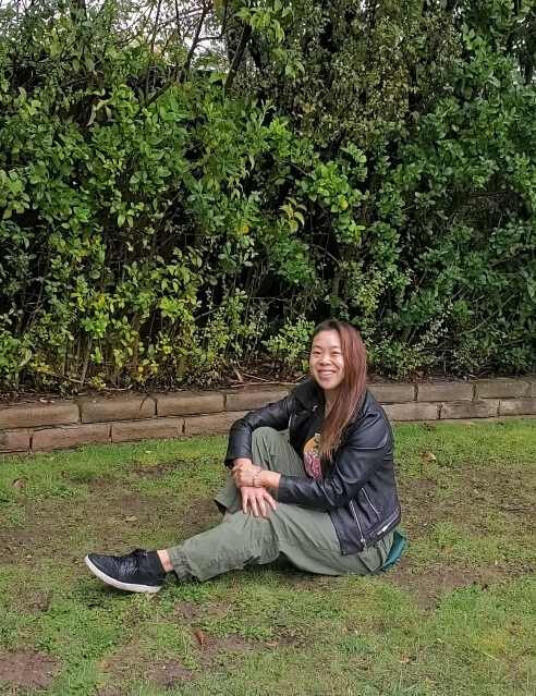 Person wearing leather jacket and green pants sitting  on the grass