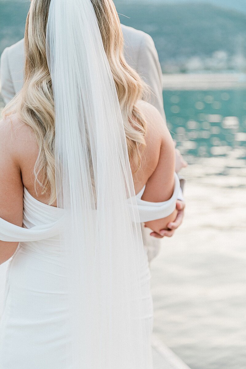 Close-up of bride in an off-shoulder gown and veil embraced by groom during a waterfront wedding moment