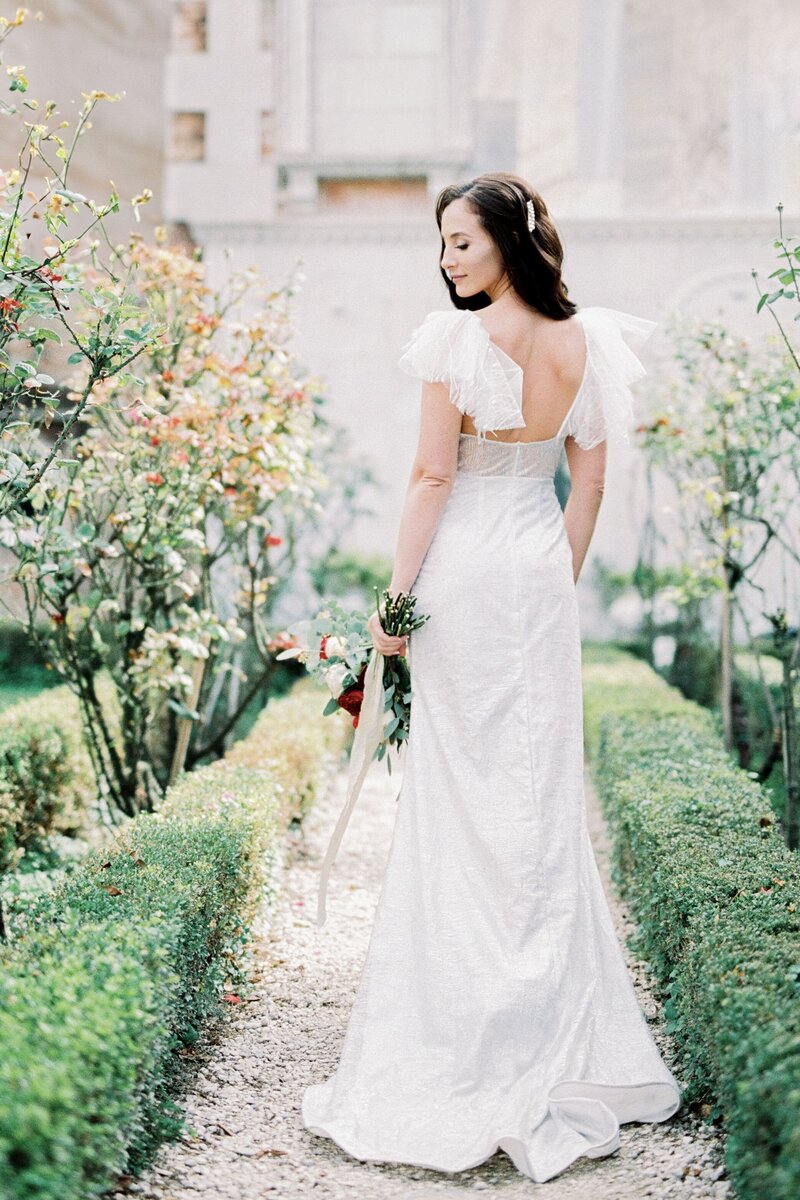 bride-white-dress-with-bouquet-flowers-stands-garden-rear-view