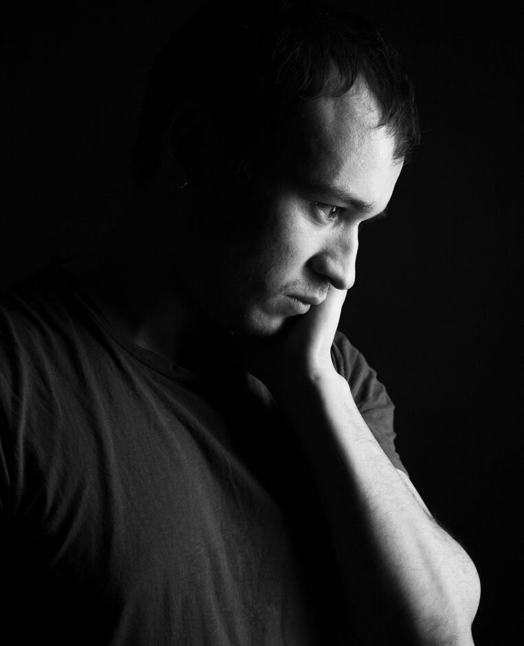 Man leaning his face on his hand looking sad, representing how a person with betrayal trauma feels after infidelity. Betrayal trauma recovery experts in the United States can help a spouse with betrayal PTSD heal and rebuild trust after infidelity.