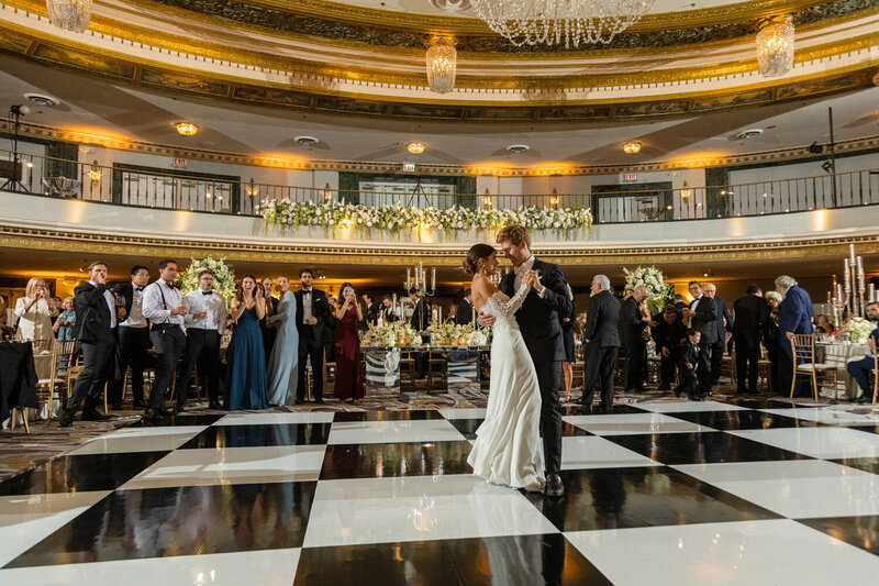 A bride and groom are dancing on a black and white checkered dance floor.