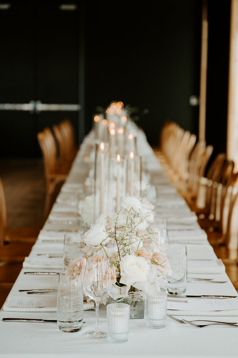 Close-up of reception table with white hydrangea, neutral roses, and bleached fern in lucite vases, styled with candlelight at Jenay and Daniel’s wedding by Summer Robbins Flowers in Central Oregon