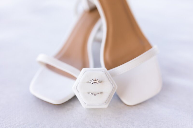 white wedding shoes stacked on heels with wedding rings in front