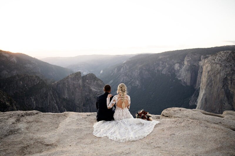 Couple sitting and admiring the view after their Yosemite elopement. Her hand on his shoulder.