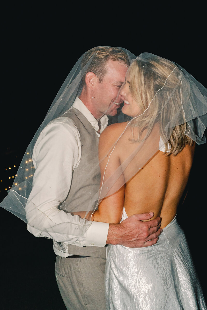 bride and groom get cozy and romantic under the bride's veil for some flash photography nighttime portraits